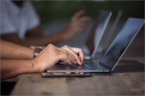 To hender skriver på et PC-tastatur, ved siden av PC-en ligger en smarttelefon.